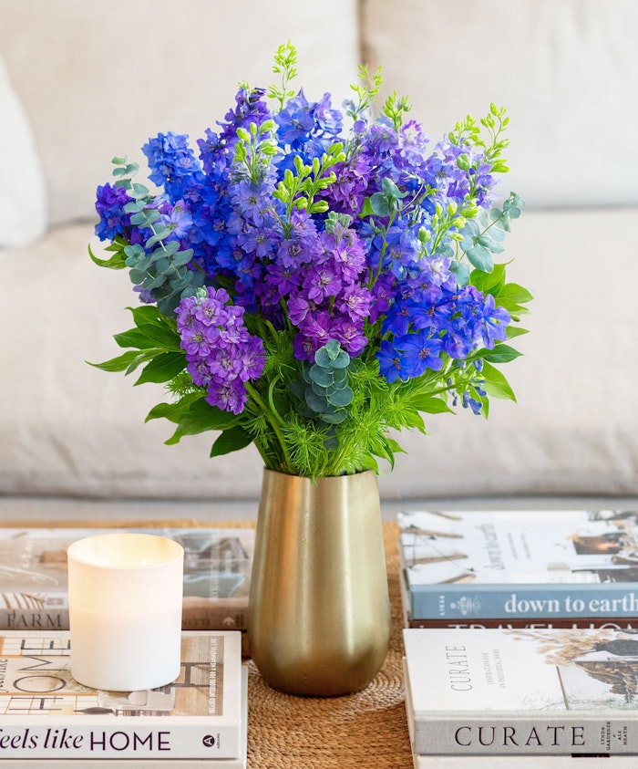 Vibrant purple floral arrangement featuring delphiniums and greenery in a stylish vase.