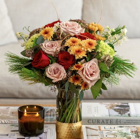 An elegant bouquet featuring pink roses, red blooms, and lush green accents on a table.