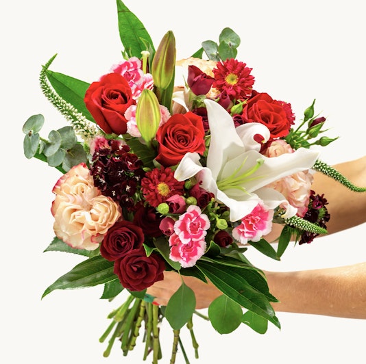 Vibrant bouquet featuring red roses, pink lilies, and assorted seasonal flowers, beautifully arranged.