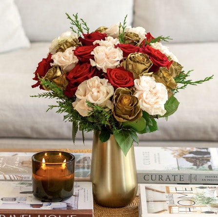 Vibrant floral arrangement featuring red, cream, and gold roses in a stylish vase.