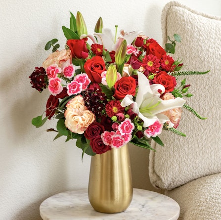 Vibrant floral arrangement featuring red roses, lilies, and pink carnations in a stylish vase.