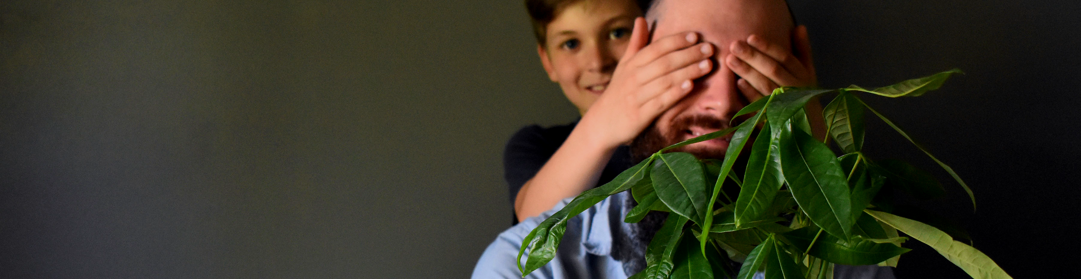A joyful moment of a boy playfully surprising his dad with a leafy plant.