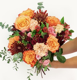 Vibrant floral bouquet featuring orange roses, pink blooms, and lush green leaves.