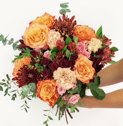 Vibrant floral bouquet featuring orange roses, pink blooms, and lush green leaves.