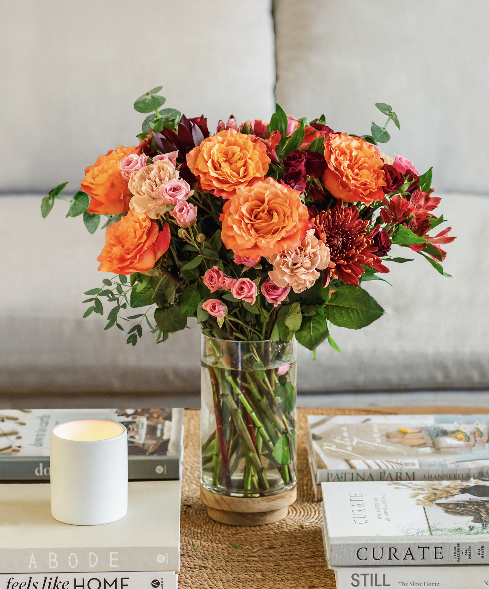 Vibrant bouquet of orange roses and pink blooms in a stylish glass vase on a coffee table.