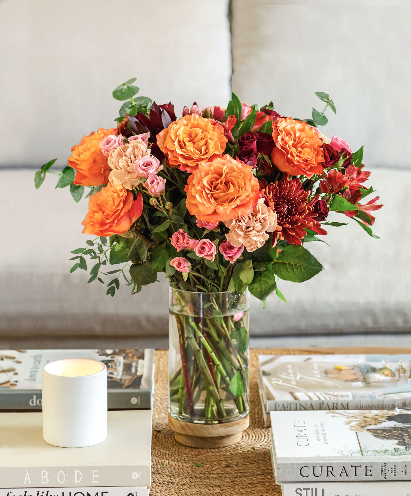 Vibrant floral arrangement featuring orange roses, pink blooms, and greenery in a glass vase.