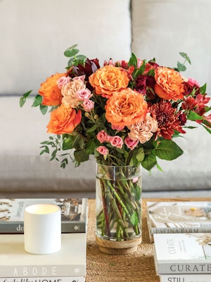 Vibrant floral arrangement featuring orange roses, pink blooms, and greenery in a glass vase.