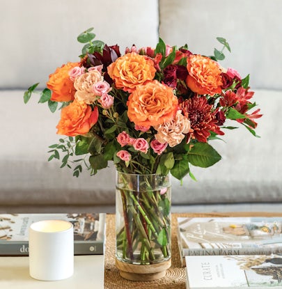 Vibrant floral arrangement featuring orange roses, pink blooms, and greenery in a glass vase.