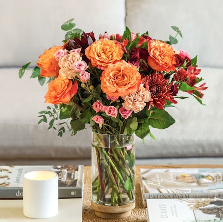 Vibrant floral arrangement featuring orange roses, pink blooms, and greenery in a glass vase.