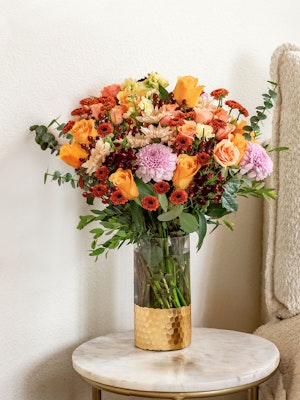 Vibrant floral arrangement featuring orange roses, chrysanthemums, and eucalyptus in a stylish vase.