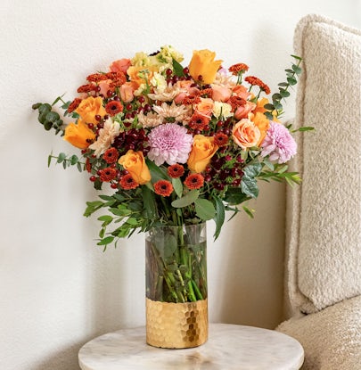 Vibrant floral arrangement featuring orange roses, chrysanthemums, and eucalyptus in a stylish vase.