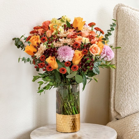 Vibrant floral arrangement featuring orange roses, chrysanthemums, and eucalyptus in a stylish vase.