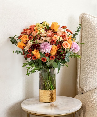 Vibrant floral arrangement featuring orange roses, chrysanthemums, and eucalyptus in a stylish vase.