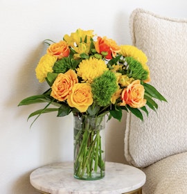 Vibrant yellow and orange floral arrangement in a glass vase, perfect for brightening up any space.