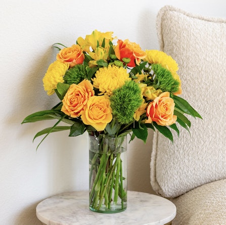 Vibrant yellow and orange floral arrangement in a glass vase, perfect for brightening up any space.