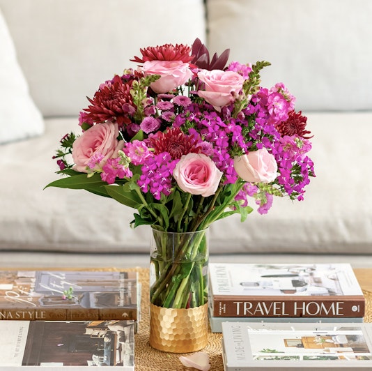 Vibrant floral arrangement with pink roses and purple blooms in a stylish vase, enhancing decor.