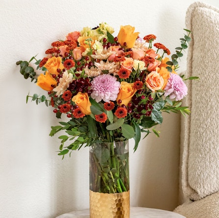 Vibrant floral arrangement featuring orange roses, pink blooms, and lush greenery in a chic vase.