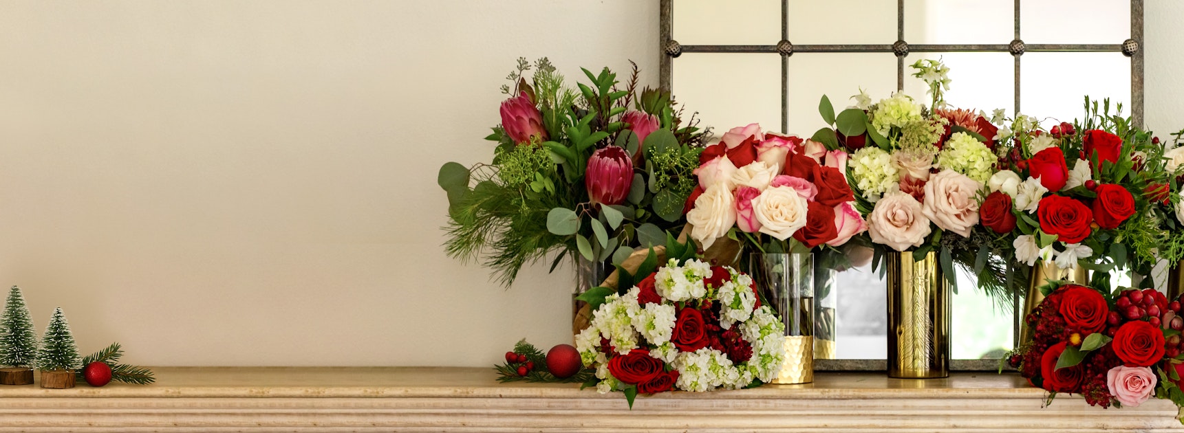 A vibrant arrangement of festive flowers in reds, pinks, and greens on a mantel.
