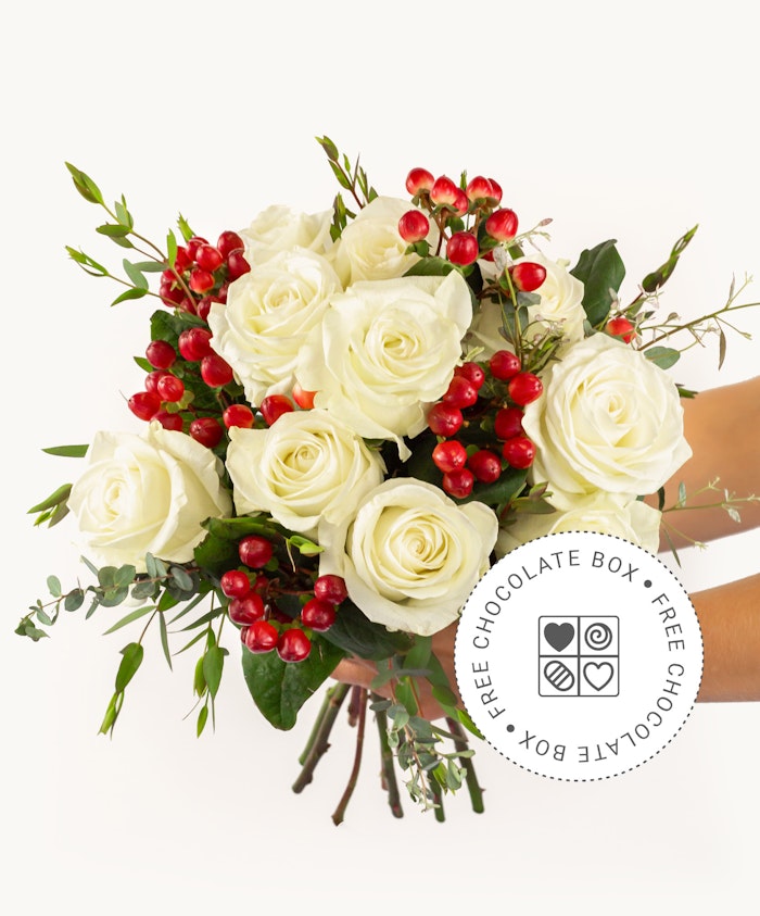 Elegant white roses paired with red berries in a lush floral arrangement, perfect for gifts.
