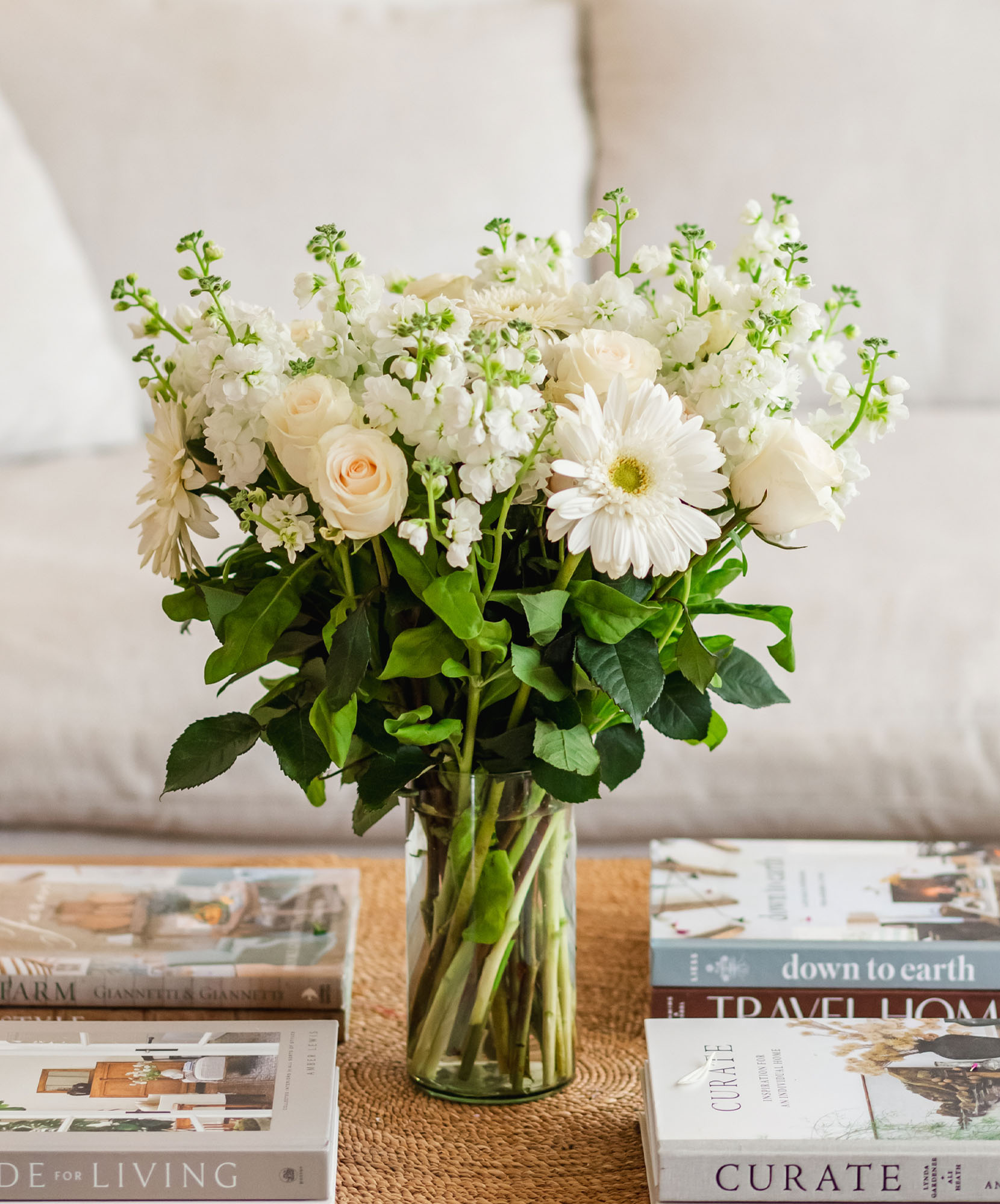 Elegant white flower bouquet featuring roses and gerbera daisies, displayed on a stylish coffee table.