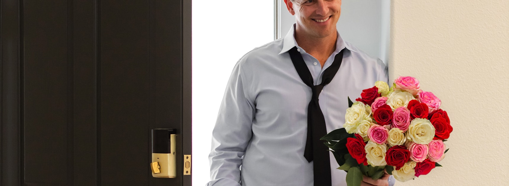 A smiling man holding a vibrant bouquet of red, pink, and white roses at his door.