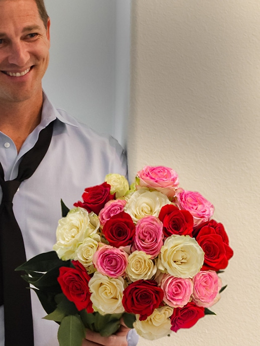 A vibrant bouquet of red, pink, and white roses held by a smiling man, perfect for any occasion.