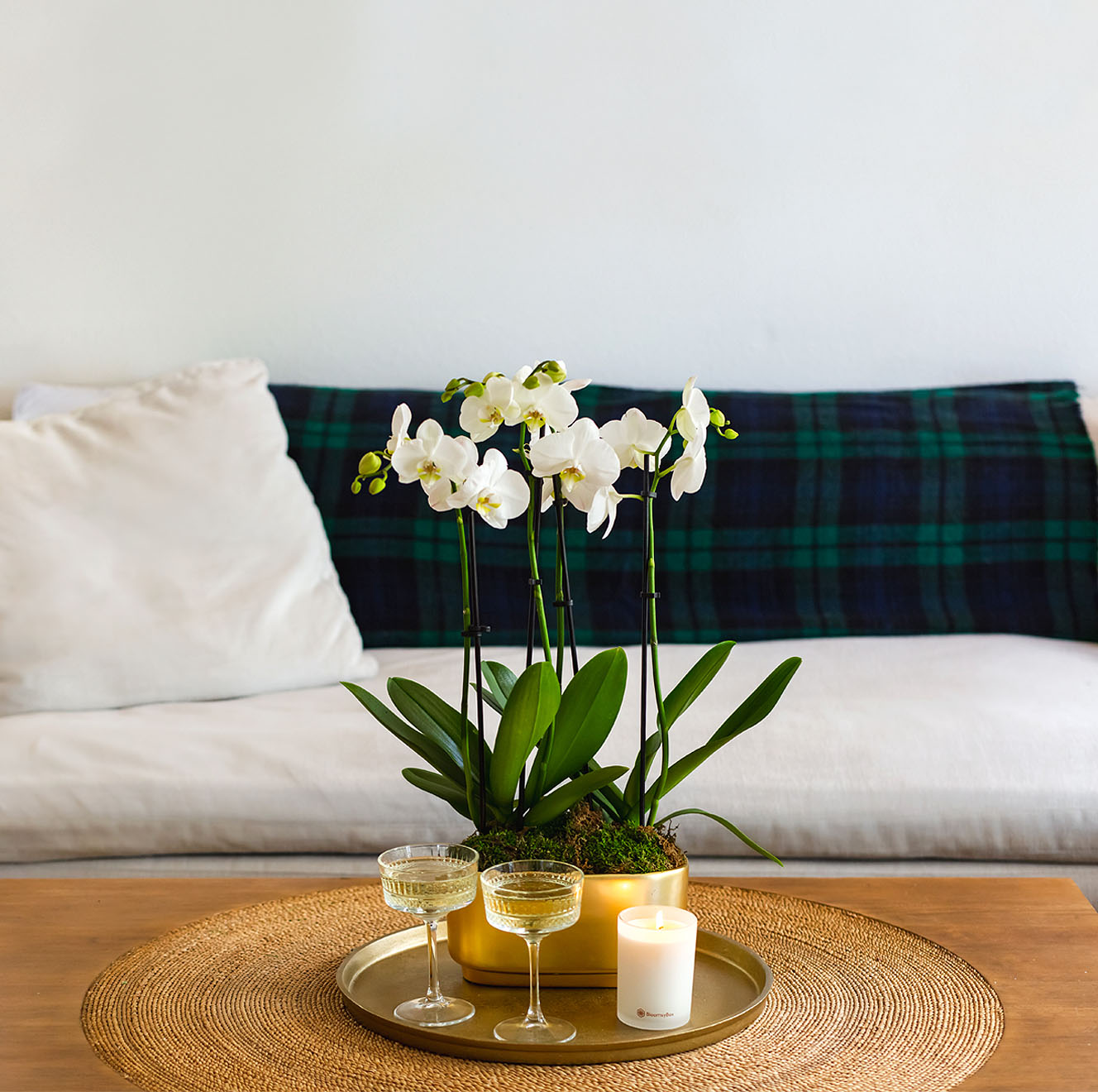 Elegant white orchids in a gold pot, complemented by candles and vintage glassware on a table.