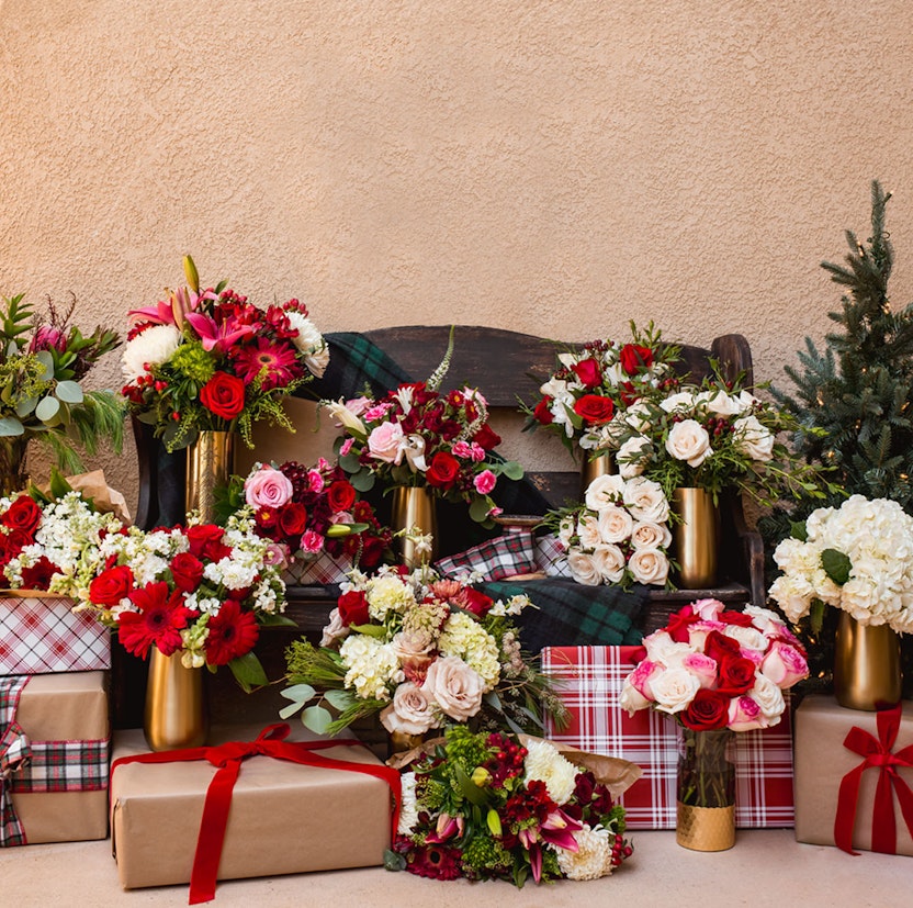 Festive floral arrangements in elegant vases surrounded by beautifully wrapped gifts.