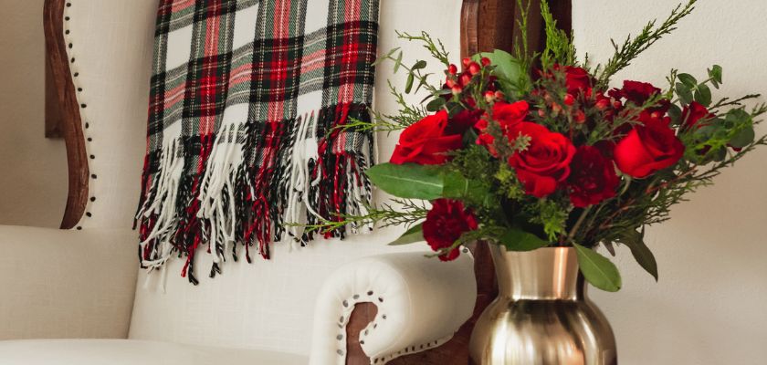 Vibrant red roses and greenery in a gold vase, set against a cozy plaid backdrop.
