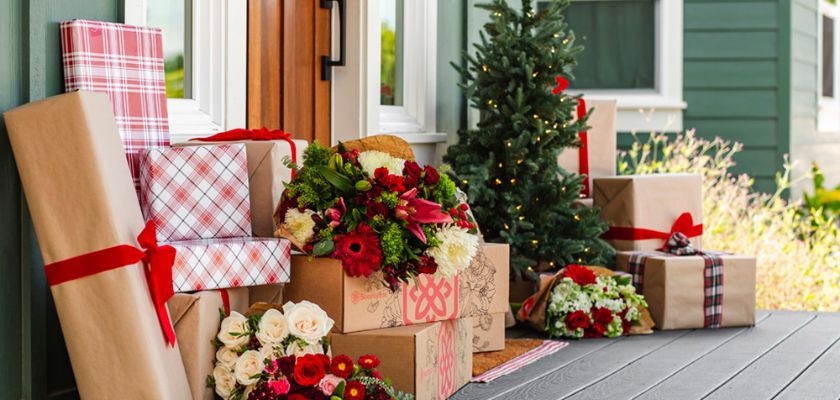 Festive holiday porch display with wrapped gifts and vibrant floral arrangements.