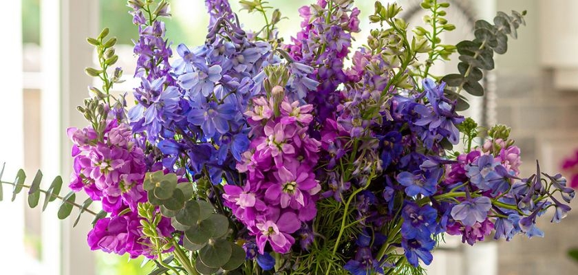 Vibrant bouquet featuring purple and blue flowers with lush greenery in a stylish arrangement.