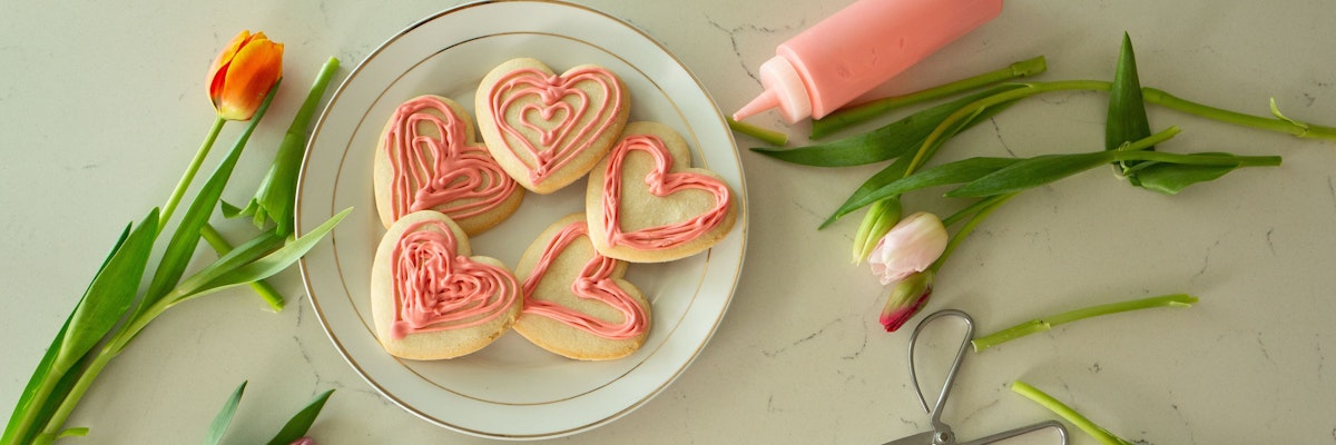 Decorative heart-shaped cookies with pink icing surrounded by fresh tulips on a marble table.