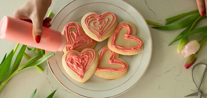 Delicious heart-shaped cookies being decorated with pink icing, perfect for celebrations.