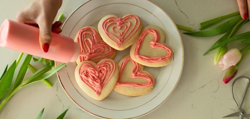 Delicious heart-shaped cookies being decorated with pink icing, perfect for celebrations.