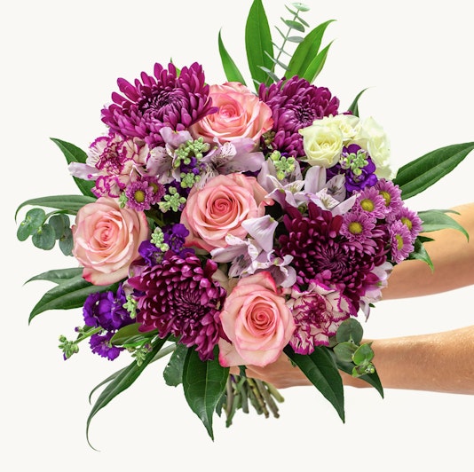 Vibrant bouquet featuring pink roses, purple chrysanthemums, and green accents, elegantly arranged.
