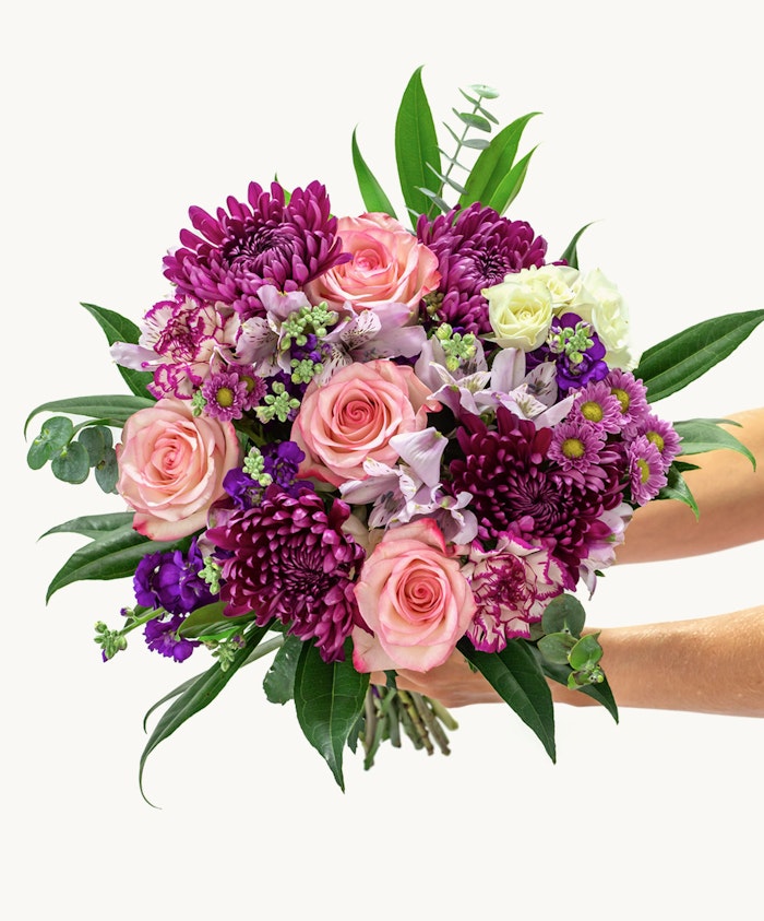 Vibrant bouquet featuring pink roses, purple chrysanthemums, and green accents, elegantly arranged.
