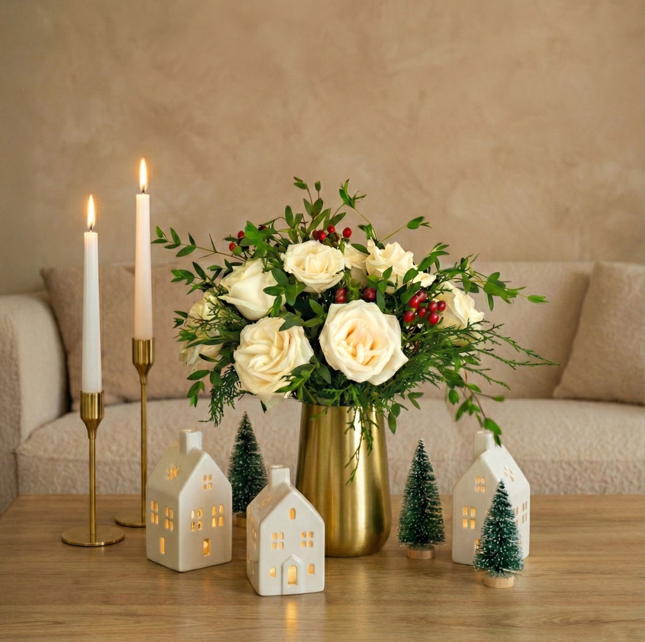 Elegant cream roses with greenery in a brass vase, surrounded by festive decorations.