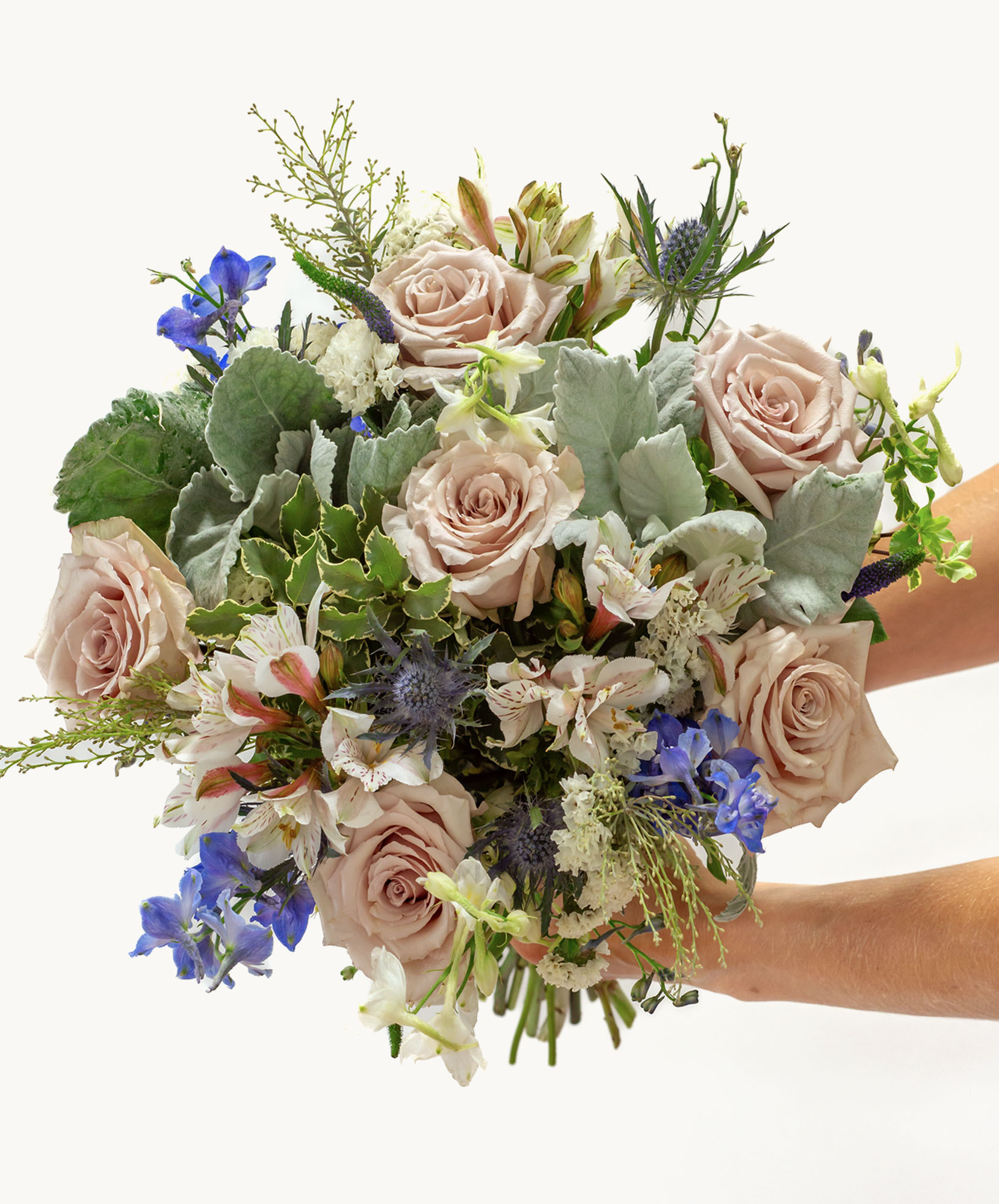 Elegant bouquet featuring soft pink roses, blue delphiniums, and lush greenery, beautifully arranged.