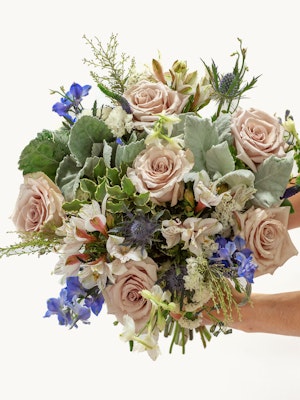 Elegant bouquet featuring soft pink roses, blue delphiniums, and lush greenery, beautifully arranged.