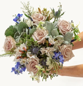 Elegant bouquet featuring soft pink roses, blue delphiniums, and lush greenery, beautifully arranged.