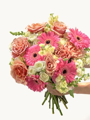 Blooming floral bouquet featuring pink gerbera daisies, roses, and delicate white blooms.
