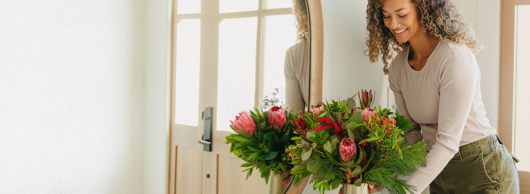 Woman with curly hair joyfully arranging a vibrant flower bouquet indoors, showcasing her floral talent.
