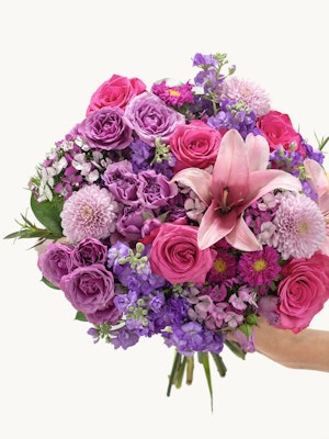 Vibrant bouquet featuring pink roses, purple lilies, and assorted blooms in a lush arrangement.