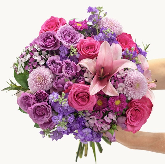 Vibrant bouquet featuring pink roses, purple lilies, and assorted blooms in a lush arrangement.