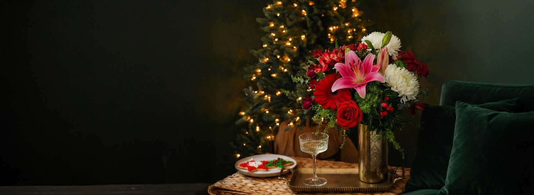 Festive floral arrangement with pink lilies and red roses, beside a decorated Christmas tree.