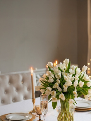 Elegant white tulip bouquet in a glass vase, set on a beautifully arranged dining table.