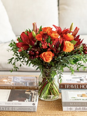 Vibrant floral arrangement with red lilies, orange roses, and lush greenery in a glass vase.