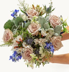 A stunning bouquet featuring blush roses, greenery, and blue florals in an elegant arrangement.