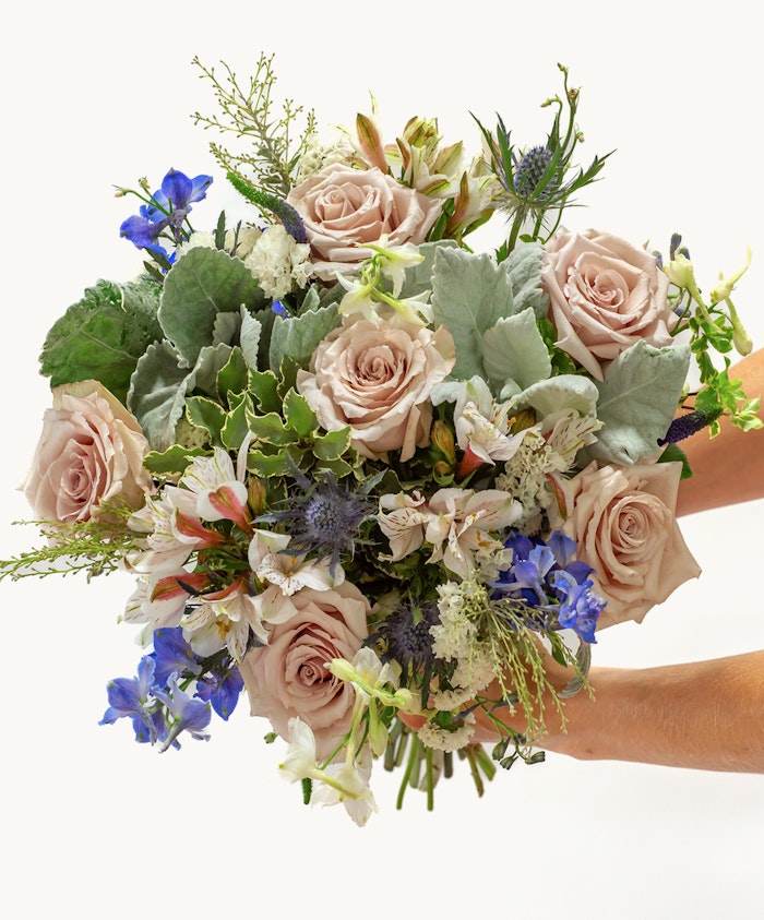 A stunning bouquet featuring blush roses, greenery, and blue florals in an elegant arrangement.