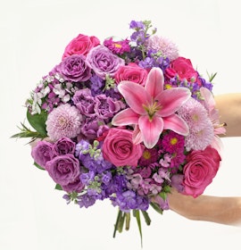 Vibrant floral bouquet featuring pink roses, lilies, and assorted purple flowers in lush arrangement.